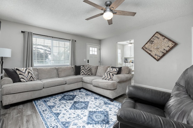 living room featuring a textured ceiling, wood finished floors, a ceiling fan, and baseboards