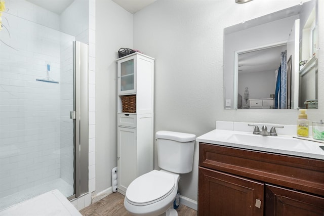 bathroom with toilet, wood finished floors, vanity, baseboards, and a shower stall