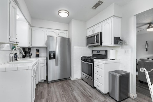 kitchen with appliances with stainless steel finishes, visible vents, a sink, and tile countertops