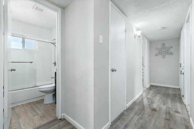 hallway featuring a textured ceiling, light wood-style flooring, visible vents, and baseboards