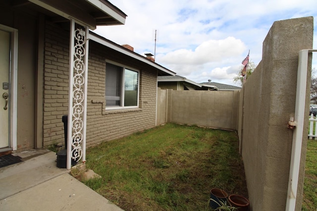view of side of property featuring brick siding, a lawn, and fence