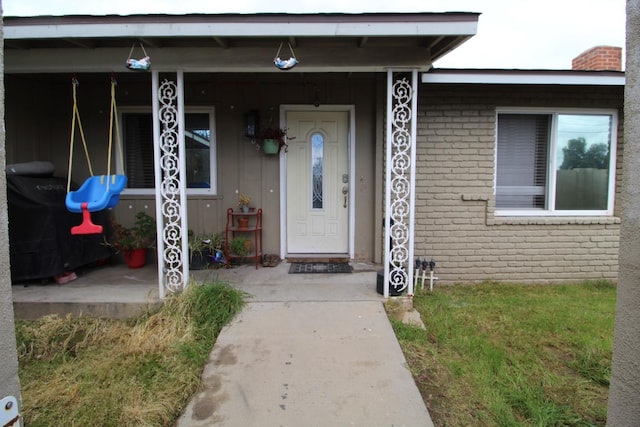 entrance to property with a porch and brick siding
