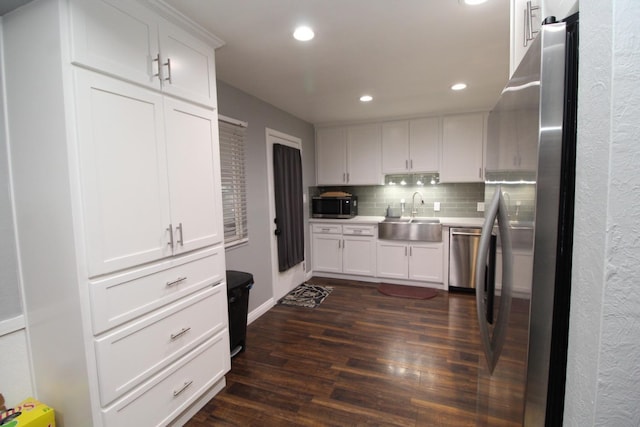 kitchen featuring dark wood-style floors, stainless steel appliances, decorative backsplash, white cabinets, and a sink