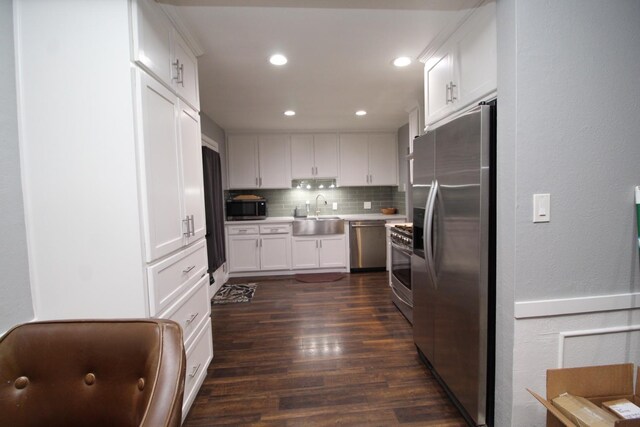 kitchen featuring stainless steel appliances, dark wood-style flooring, a sink, white cabinets, and backsplash