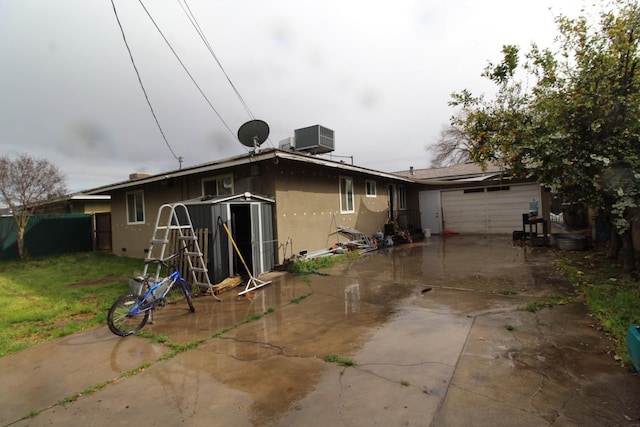 back of house featuring a patio, stucco siding, an attached garage, central AC, and driveway