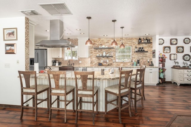 kitchen with a breakfast bar area, open shelves, tasteful backsplash, visible vents, and island range hood