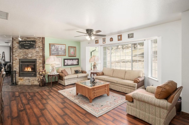 living room featuring ceiling fan, a textured ceiling, a stone fireplace, dark wood-style flooring, and visible vents