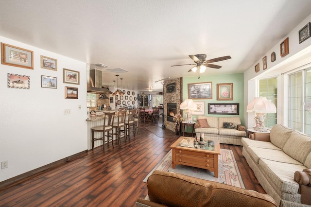 living room featuring a large fireplace, ceiling fan, baseboards, and dark wood finished floors