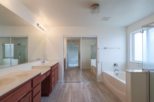 bathroom featuring a textured ceiling, a garden tub, wood finished floors, visible vents, and double vanity