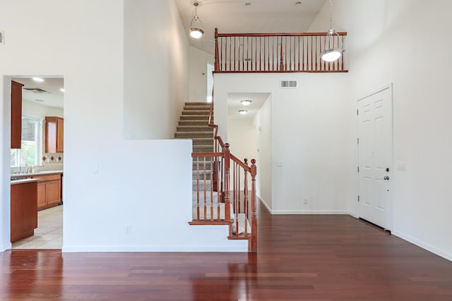 stairs featuring baseboards, visible vents, a high ceiling, and wood finished floors