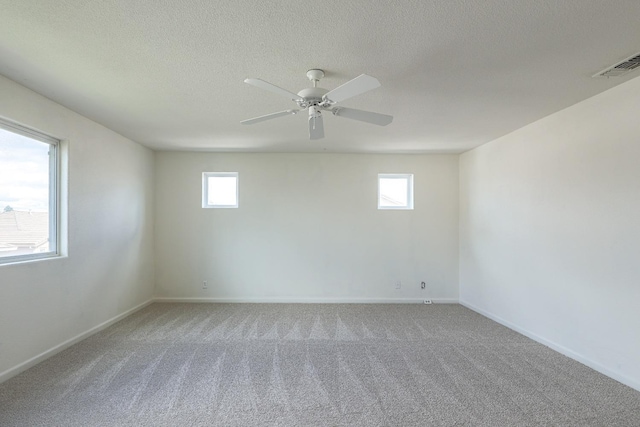 carpeted empty room with a textured ceiling, ceiling fan, visible vents, and baseboards