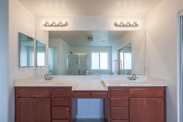 bathroom with a sink, a shower stall, a textured ceiling, and double vanity