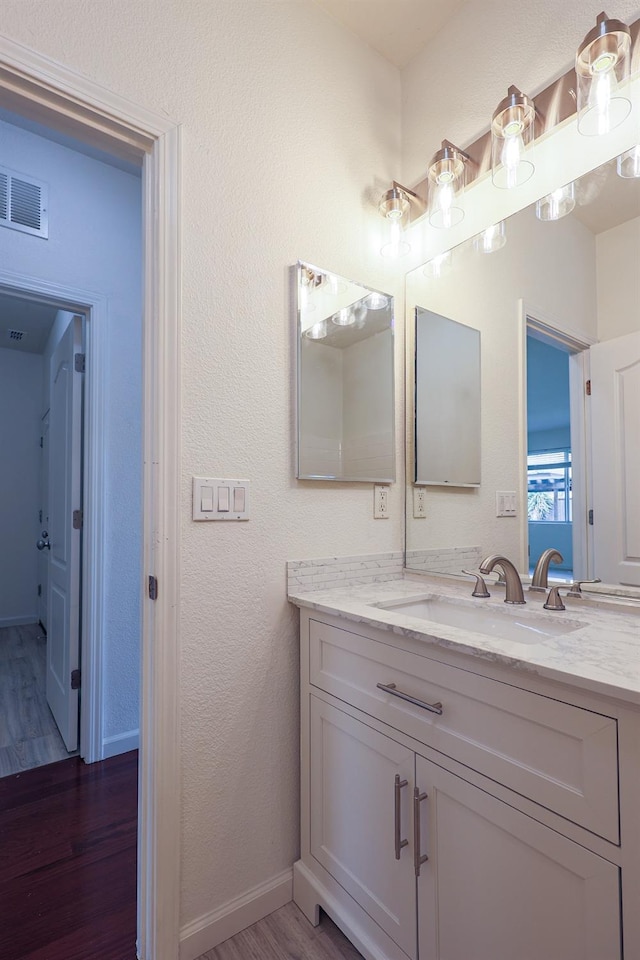 bathroom featuring baseboards, visible vents, a textured wall, wood finished floors, and vanity