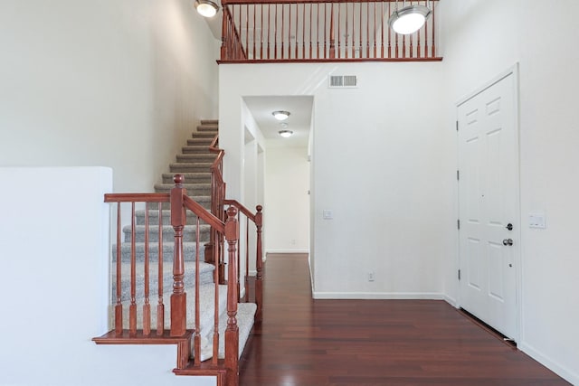 entryway with visible vents, a towering ceiling, wood finished floors, baseboards, and stairs