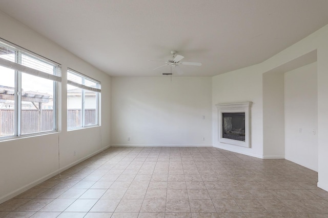 unfurnished room featuring a ceiling fan, a glass covered fireplace, baseboards, and light tile patterned floors