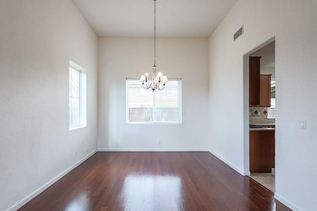 unfurnished dining area with visible vents, a notable chandelier, baseboards, and wood finished floors