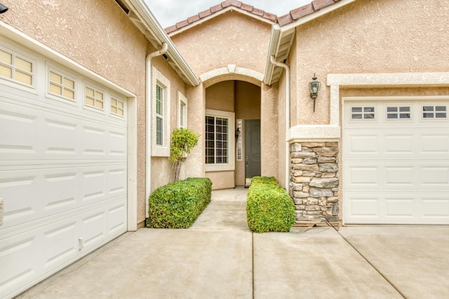 property entrance with a garage, stone siding, a tile roof, and stucco siding