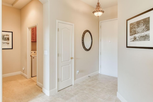 hallway with washer / clothes dryer, light carpet, baseboards, and light tile patterned floors