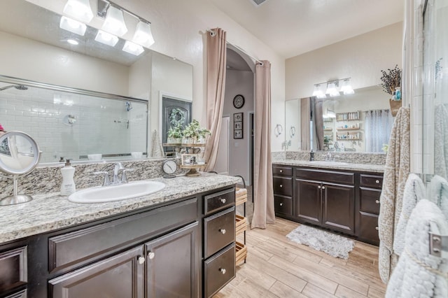 bathroom featuring two vanities, a sink, a shower stall, and wood finished floors