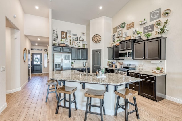 kitchen featuring stainless steel appliances, a breakfast bar area, a towering ceiling, and light wood-style flooring