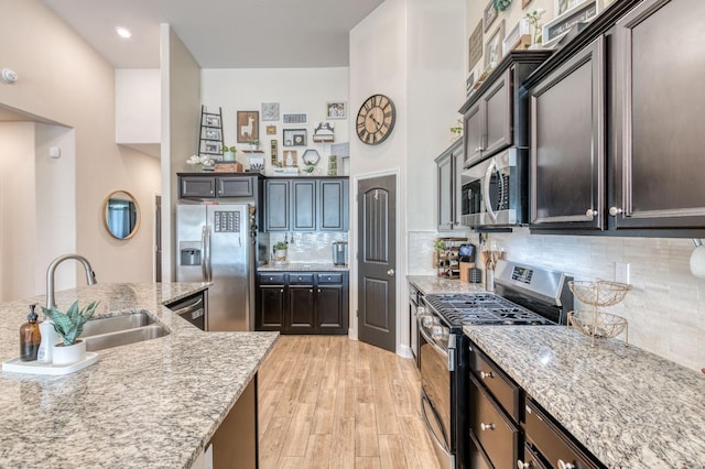 kitchen featuring light stone counters, light wood finished floors, decorative backsplash, appliances with stainless steel finishes, and a sink