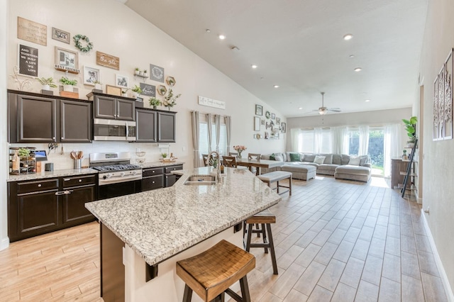 kitchen with a breakfast bar area, stainless steel appliances, a sink, light stone countertops, and light wood finished floors