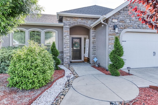 entrance to property featuring a garage, stone siding, roof with shingles, and stucco siding