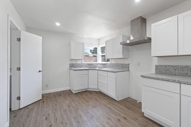 kitchen featuring light wood-type flooring, wall chimney exhaust hood, baseboards, and white cabinets