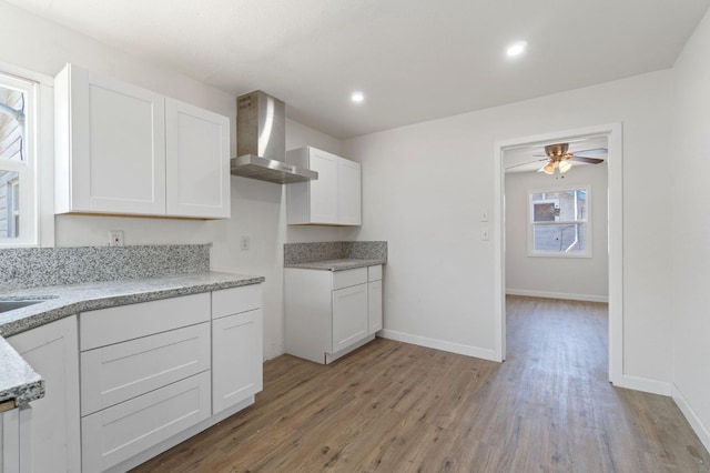 kitchen with baseboards, white cabinets, wall chimney exhaust hood, light wood-type flooring, and recessed lighting