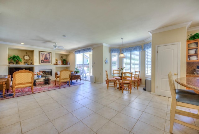 interior space featuring light tile patterned floors, baseboards, a tile fireplace, ceiling fan, and crown molding