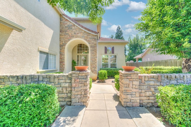 property entrance with stone siding, a patio area, fence, and stucco siding