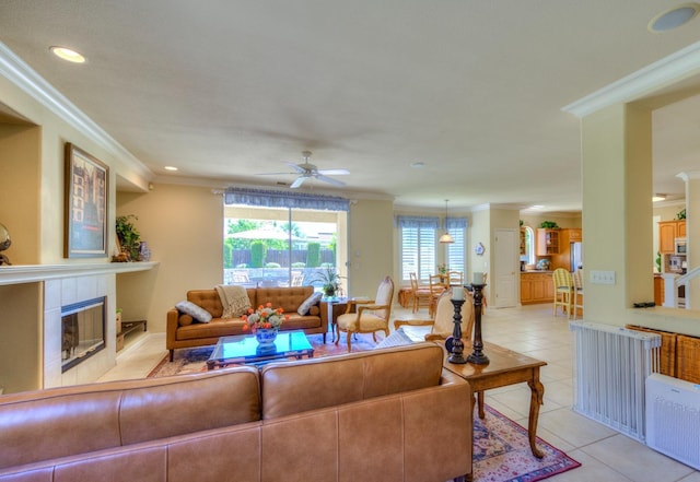 living area featuring light tile patterned floors, ceiling fan, a tile fireplace, and crown molding