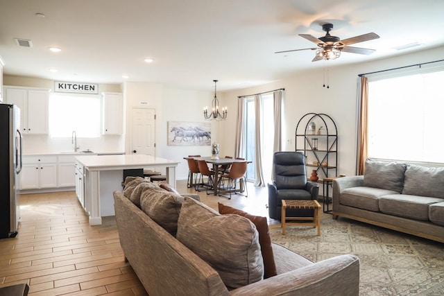 living room with light wood-style flooring, ceiling fan with notable chandelier, visible vents, and recessed lighting