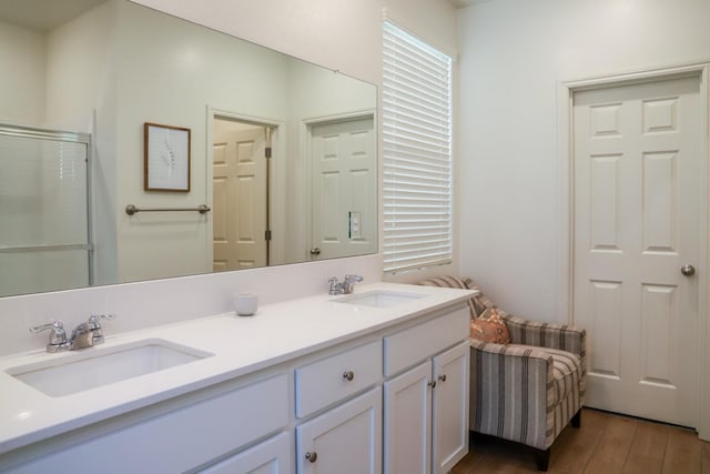 bathroom with double vanity, a shower with shower door, a sink, and wood finished floors