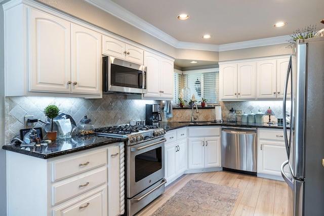 kitchen featuring white cabinets, crown molding, stainless steel appliances, and a sink