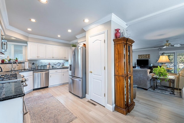 kitchen with appliances with stainless steel finishes, white cabinets, light wood finished floors, and decorative backsplash