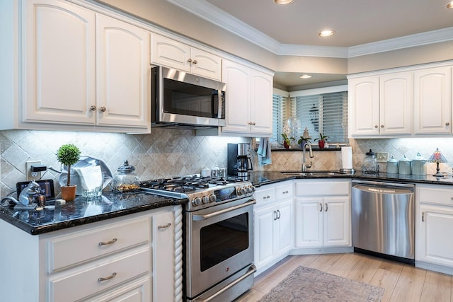 kitchen with a sink, white cabinetry, ornamental molding, appliances with stainless steel finishes, and dark stone countertops