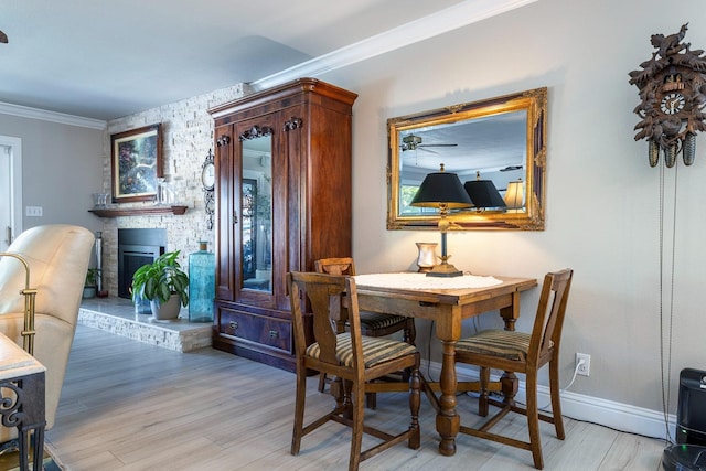 dining space featuring ornamental molding, light wood-style floors, a fireplace, and baseboards