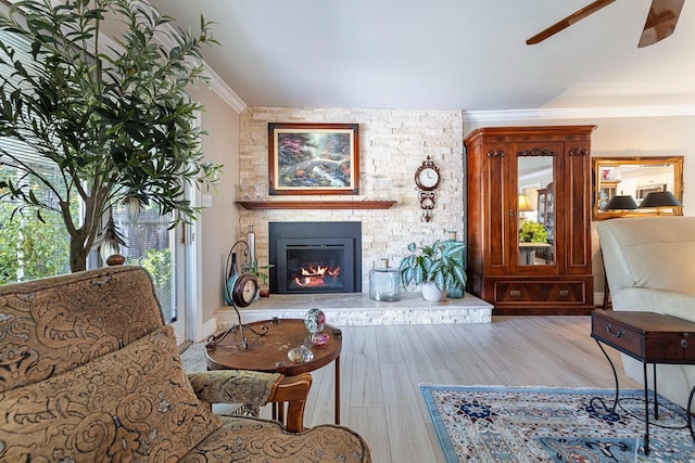 living room featuring a stone fireplace, ornamental molding, wood finished floors, and a ceiling fan