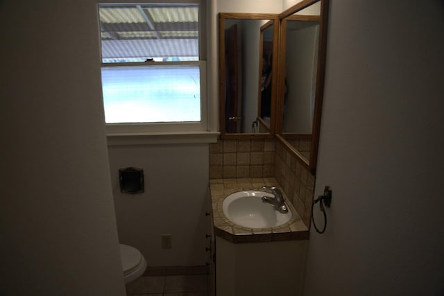 half bath with toilet, tasteful backsplash, vanity, and tile patterned floors