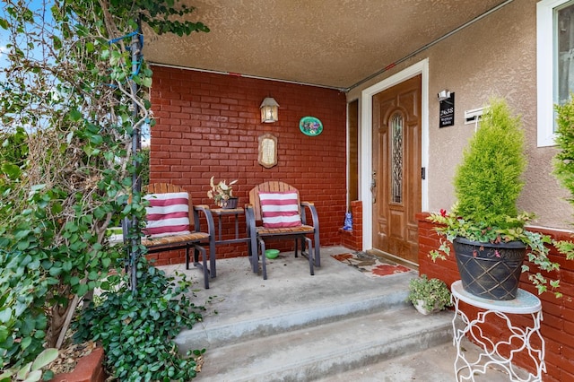 property entrance with a porch, brick siding, and stucco siding