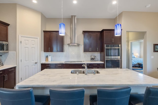 kitchen featuring a sink, dark brown cabinets, wall chimney range hood, appliances with stainless steel finishes, and a kitchen bar