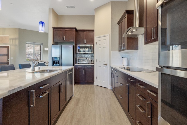 kitchen with stainless steel appliances, wall chimney exhaust hood, a sink, and light countertops