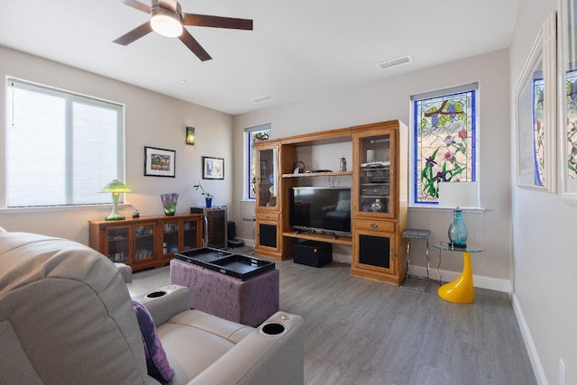 living area featuring a ceiling fan, plenty of natural light, baseboards, and wood finished floors