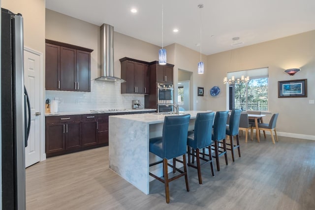 kitchen with decorative backsplash, freestanding refrigerator, wall chimney range hood, dark brown cabinets, and stovetop