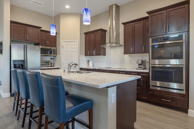 kitchen with tasteful backsplash, visible vents, wall chimney exhaust hood, stainless steel appliances, and a sink