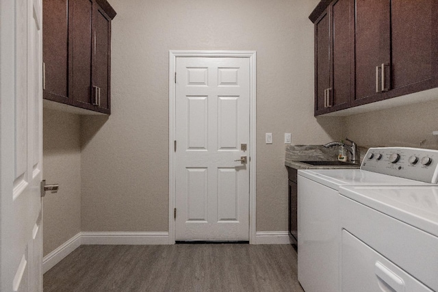 washroom featuring wood finished floors, a sink, baseboards, cabinet space, and washer and clothes dryer