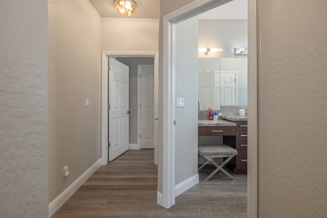 corridor with dark wood-style flooring, a textured wall, and baseboards