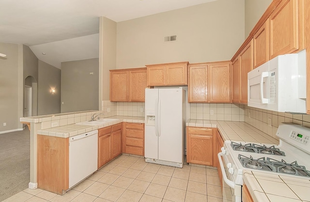 kitchen featuring a peninsula, white appliances, visible vents, and tile counters