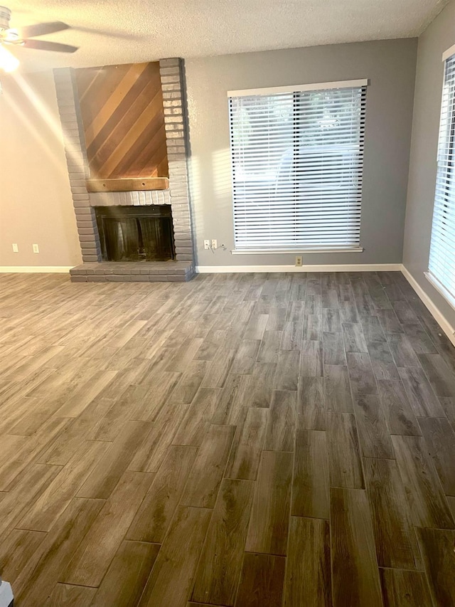 unfurnished living room with a brick fireplace, a textured ceiling, baseboards, and dark wood-style flooring